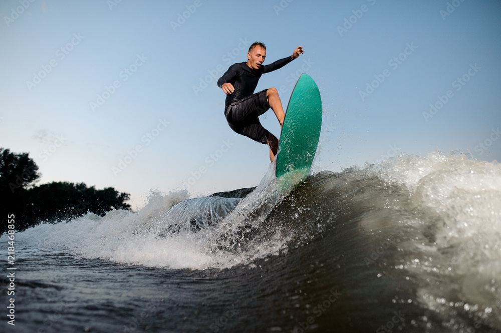 Active and young wake surfer jumping on a wake board down the river