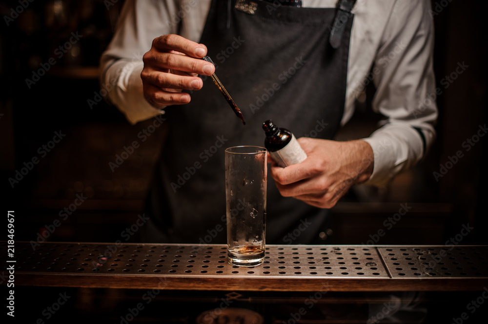 Barman adding brown bitter into a cocktail glass