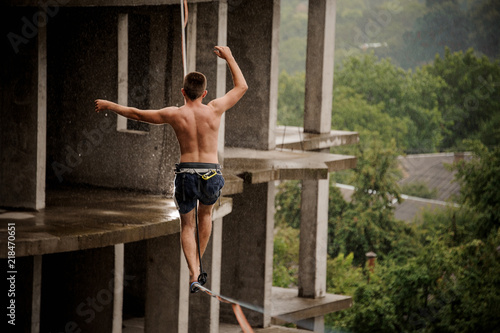 Back view of young brave topless man walking on a slackline