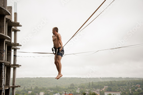 Athletic brave man balancing on a slackline against the grey sky