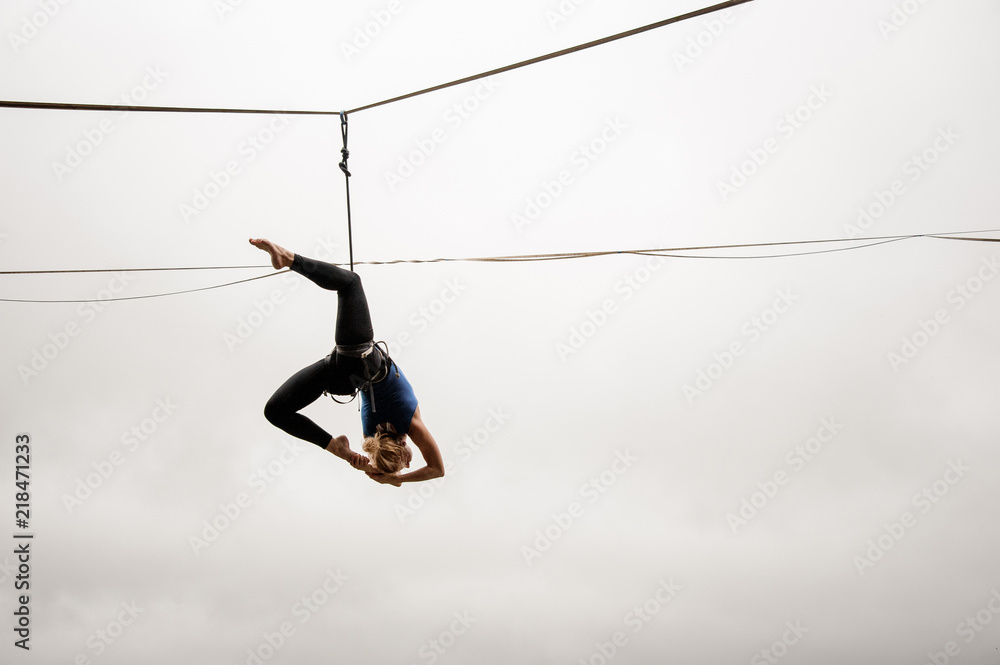 Brave slim blonde girl balancing on a slackline against the grey sky