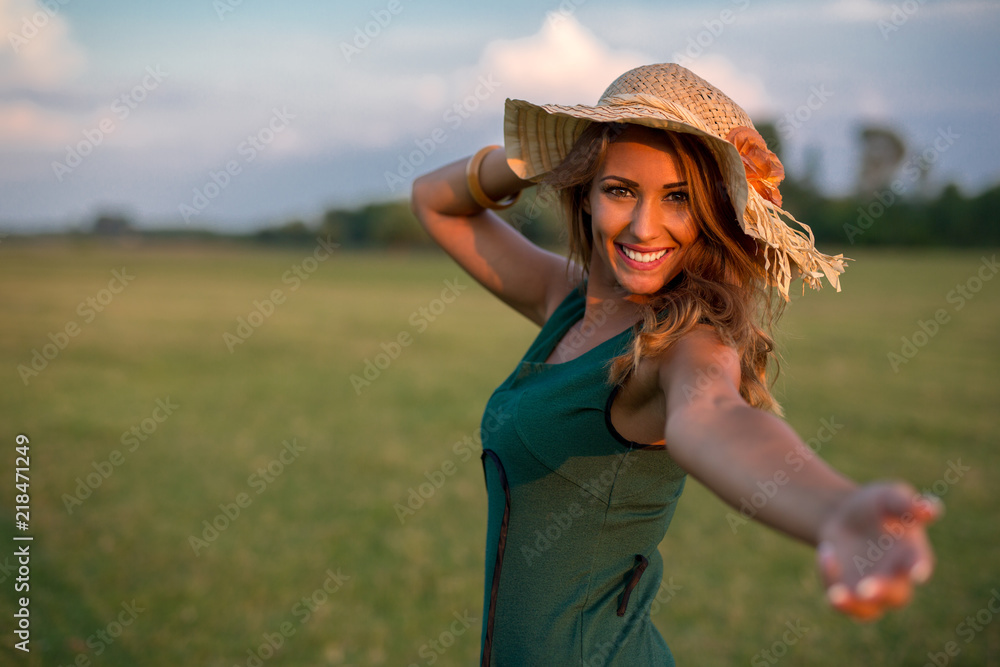 Beautiful young happy woman reaching her hand in a field while smiling
