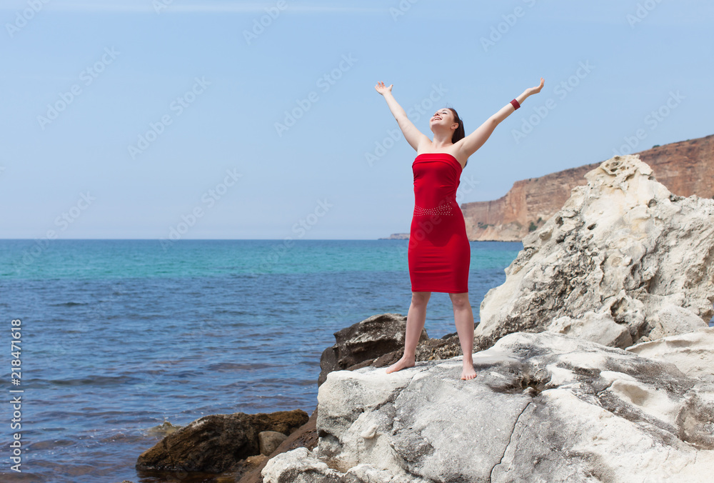 Female person in red sundress on wild rocky seashore Female person in red sundress on wild rocky seashore