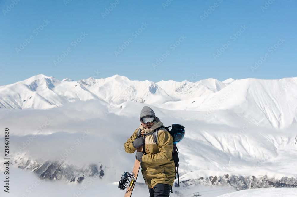 guy with a wooden snowboard in his hands stands on the backdrop of mountains
