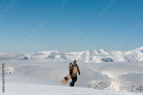 male wearing glasses and snowboard walking in the snow against the backdrop of the mountains