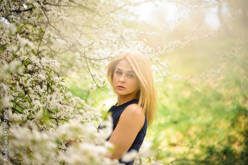 Tender blonde woman standing on the blurred background of a white blooming cherry tree