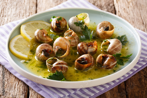 Delicatessen food: edible snails, escargot cooked with butter, parsley, lemon and garlic close-up on the table. horizontal photo