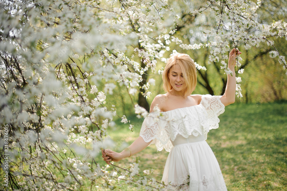 Happy young blonde woman in white dress walking among white blooming cherry trees Happy young blonde woman in white dress walking among white blooming cherry trees