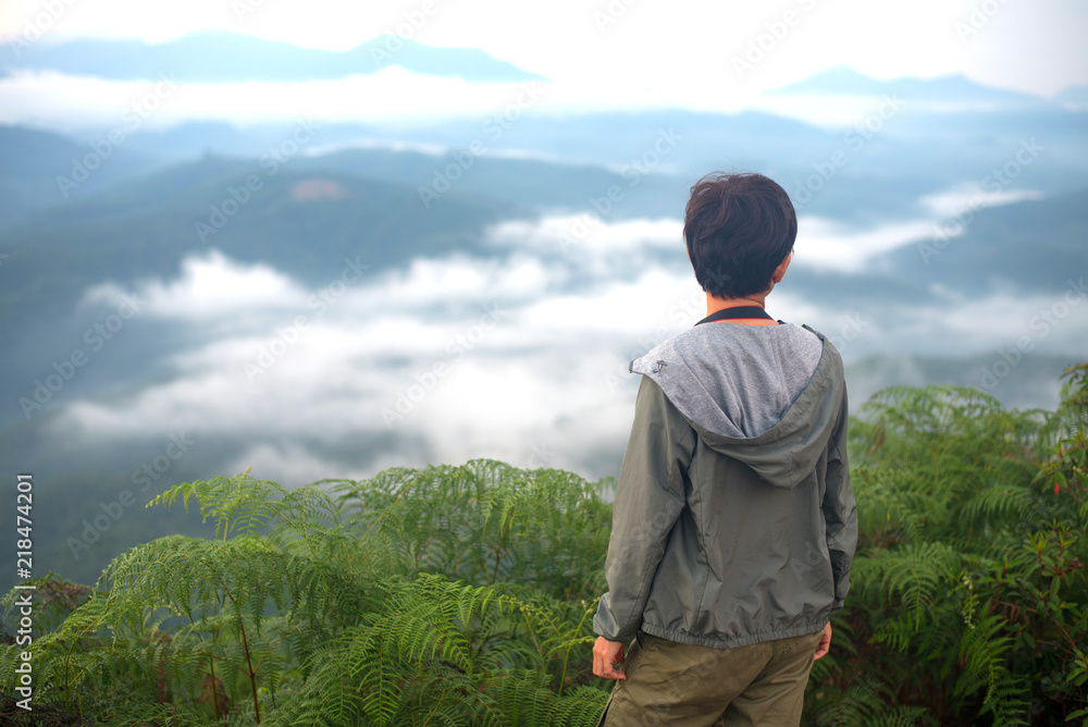 Naklejka premium Tourist woman standing on peak of mountains and enjoy view with beautiful mist and sunrise from her success at Gunungsilepat mountains, Yala province south of Thailand.