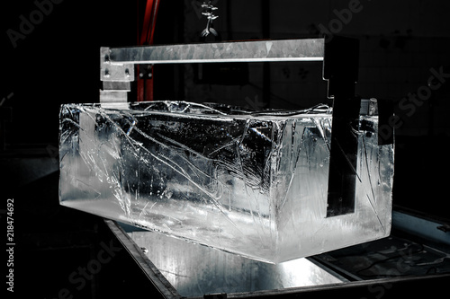 Fotografi Steel tool holding a huge ice cube on dark background of modern factory