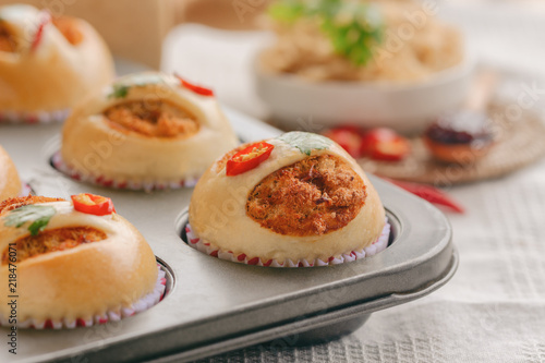 Homemade cup of soft and sticky bun with dried shredded pork or pork floss and shrimp roasted chili paste in muffin tray on wood table. Thai style delicious bread with sweet and spicy taste for snack.