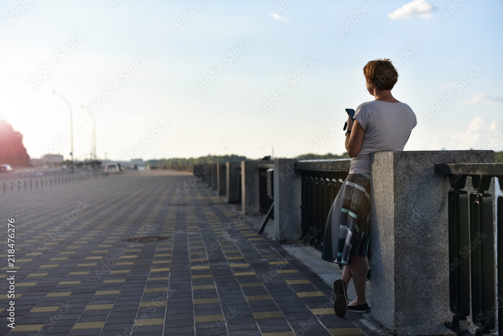 woman alone on city embankment hold telephone and looking on sunset woman alone on city embankment hold telephone and looking on sunset