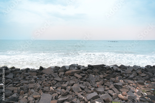 Rocky beach with black brown stones and waves dashing into them. Shot at sunset during a cloudy day with the red sky of sunset. This is promenade beach in pondicherry a famous tourist spot