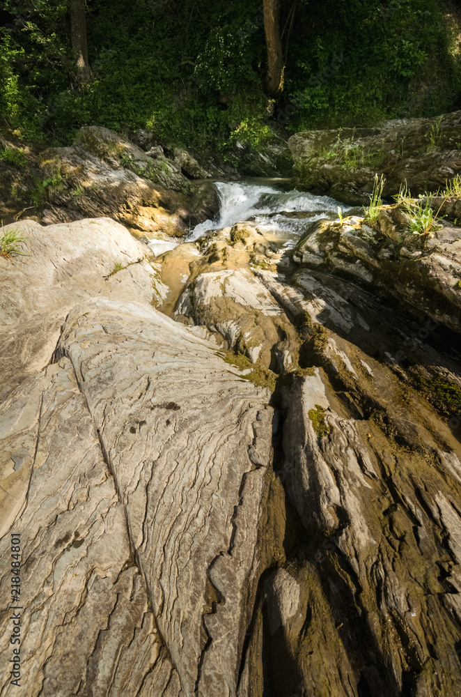 Wide angle shot of mountain river with a waterfall flowing between rocky coasts. Expressive foreground. Taken from low point of view at sunny spring day at Carpathian mountains. Natural background. 
