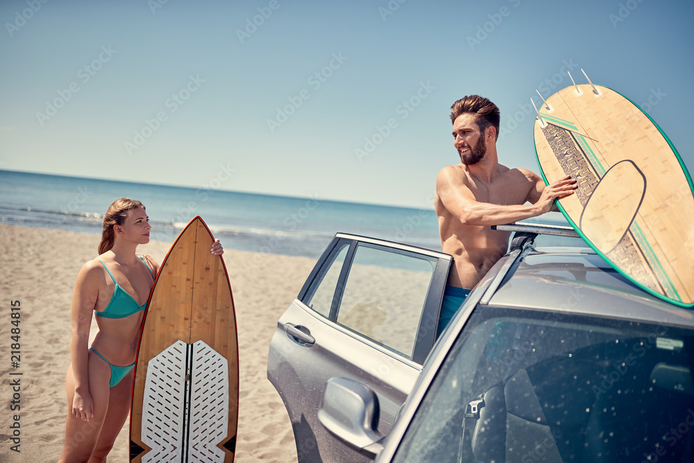 Summer holiday road trip vacation- surfer couple at the beach getting ready for surfing.