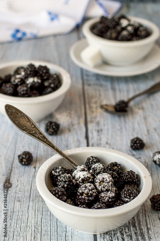 Fresh blackberries with sugar powder in small round cups on an old wooden table. Fresh blackberries with sugar powder in small round cups on an old wooden table.