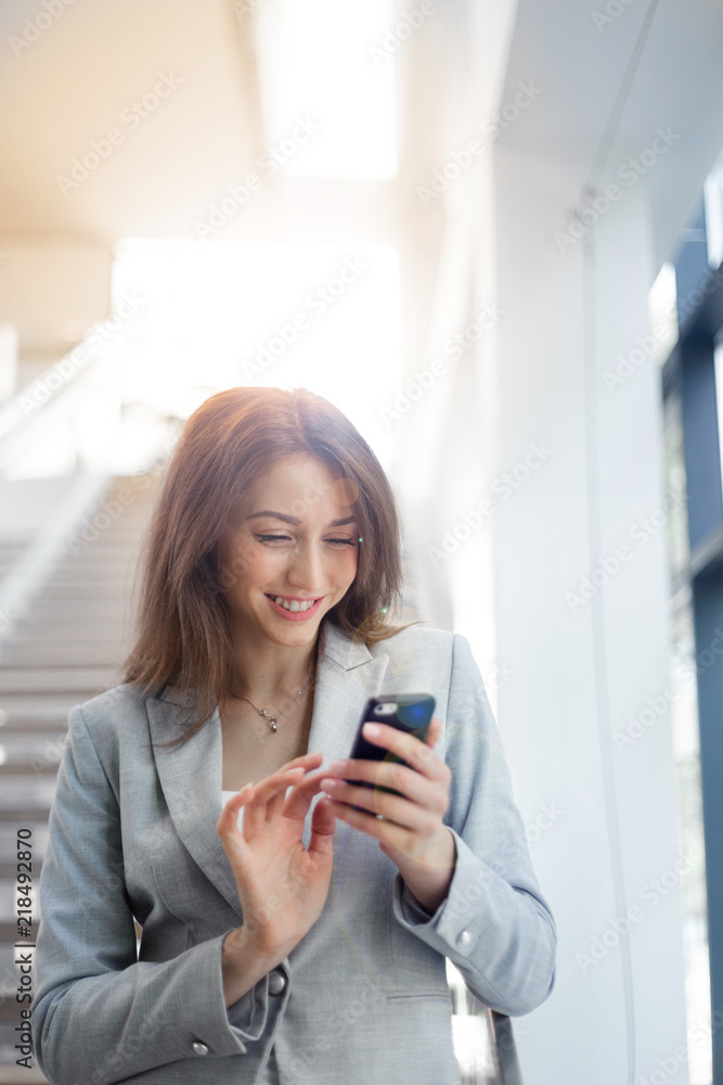 Young smiling businesswoman using a smartphone standing on stairs , communication, people and technology concept, copy space Young smiling businesswoman using a smartphone standing on stairs , communication, people and technology concept, copy space