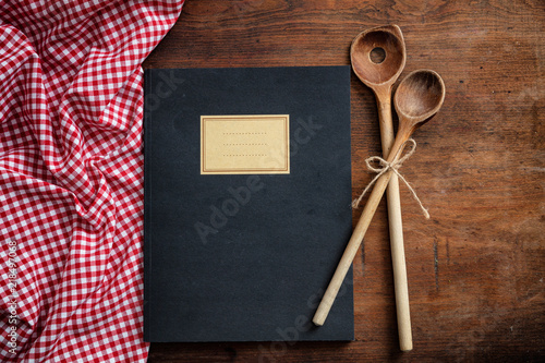 Notebook, kitchen utensils and red tablecloth on wooden table, top view
