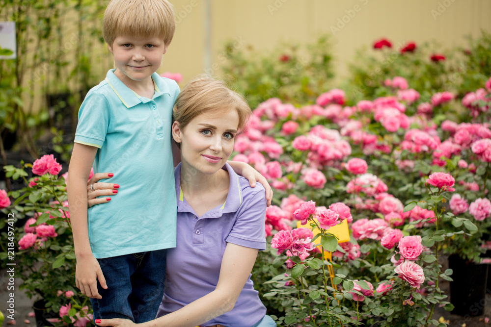 Caucasian woman with blond short hair and blue eyes poses with her six year old son over rose garden background.
