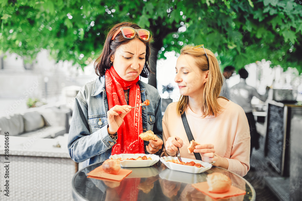 Two girl friends students trying sausage with grimace of disgust on their face. The concept of spoiled fast food Two girl friends students trying sausage with grimace of disgust on their face. The concept of spoiled fast food