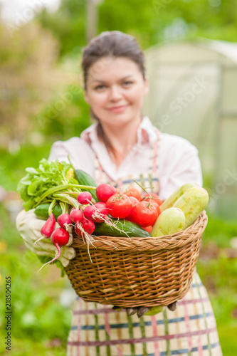 Happy woman with fresh vegetables in the basket in her hands. Focused on vegetable