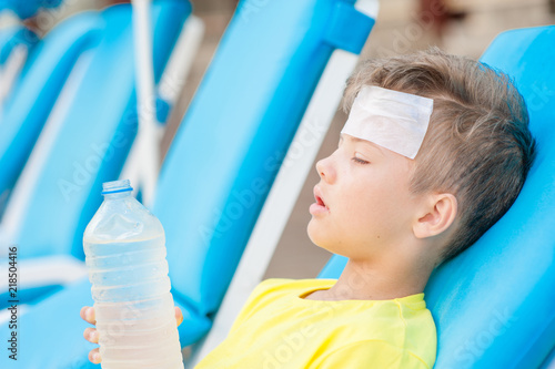 Little boy on the beach with a sunstroke holds a bottle of water photo