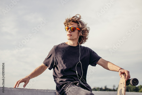 Schilderij op canvas stylish young man with skateboard listening music with headphones , near concret