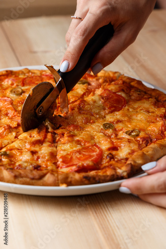 People Hands cutting homemade pizza. Hand slicing a homemade pizza with a cutter on a wooden table