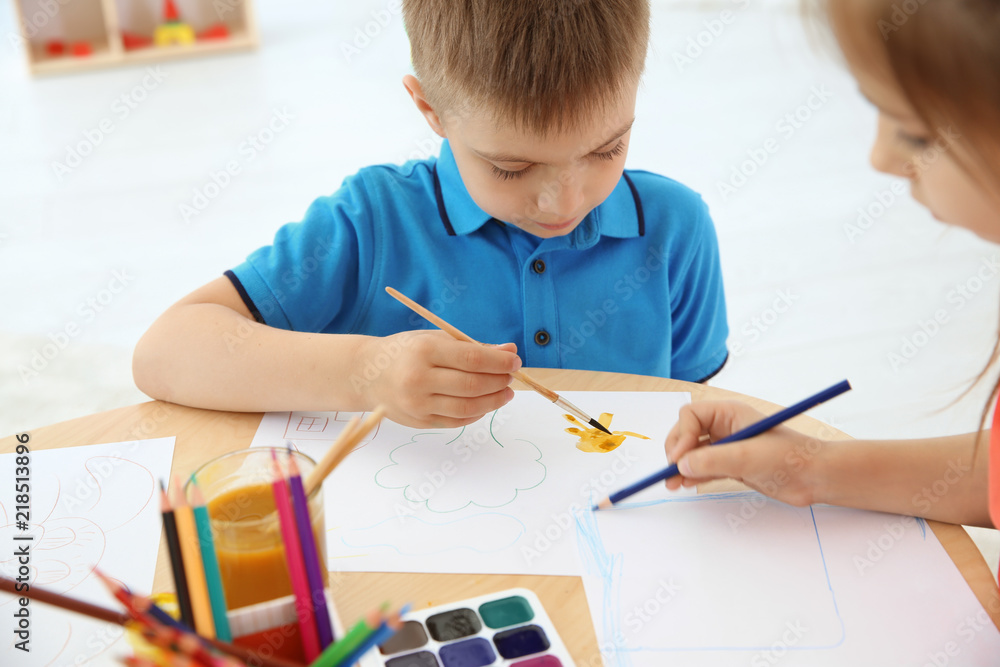 Cute little children painting at table in playing room Cute little children painting at table in playing room