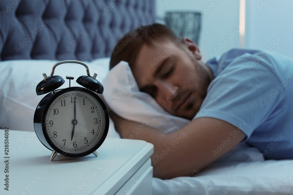 Alarm clock on table and young man sleeping in bed at night Stock Photo |  Adobe Stock