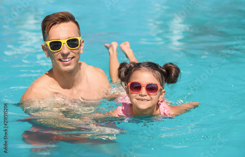 Young man teaching his daughter to swim in pool