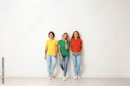 Group of young women in jeans and colorful t-shirts near light wall