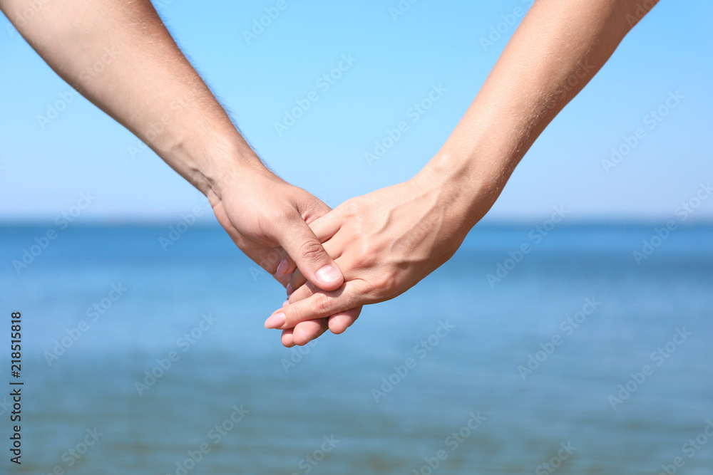 Happy couple holding hands at beach on sunny day, closeup Happy couple holding hands at beach on sunny day, closeup