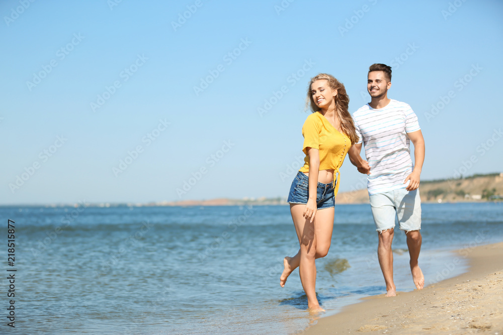 Happy young couple walking at beach on sunny day