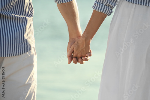 Happy young couple holding hands on beach, closeup