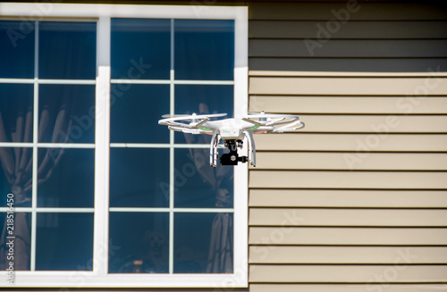 white drone with camera hovering by house window