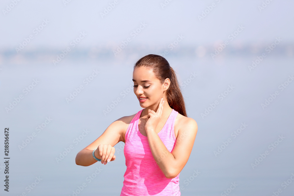 Young woman checking pulse outdoors on sunny day