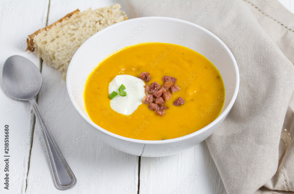 Butternut and bacon soup with sour cream, bacon bits and scallion topping in white bowl on white rustic table Butternut and bacon soup with sour cream, bacon bits and scallion topping in white bowl on white rustic table