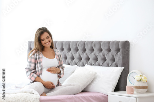Happy pregnant woman sitting on bed at home