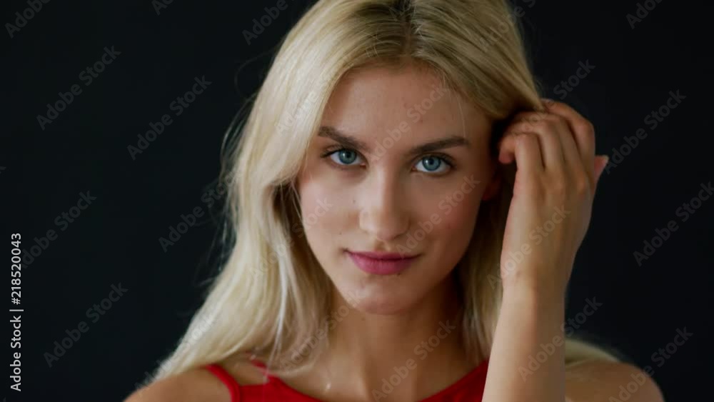 Charming young woman with blue eyes smiling and looking at camera while standing on black background Charming young woman with blue eyes smiling and looking at camera while standing on black background