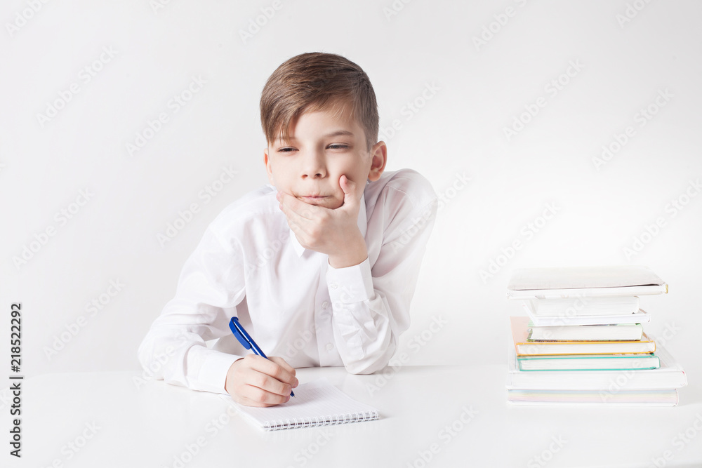 Pensive school boy writes in notebook at the table Pensive school boy writes in notebook at the table