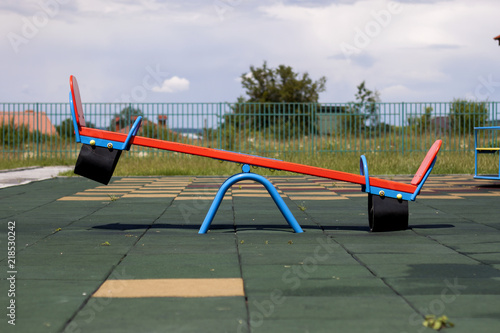 Photography New modern plastic bright colorful blue and red empty toy seesaw swing on nursery playground with soft rubber flooring on bright sunny summer day