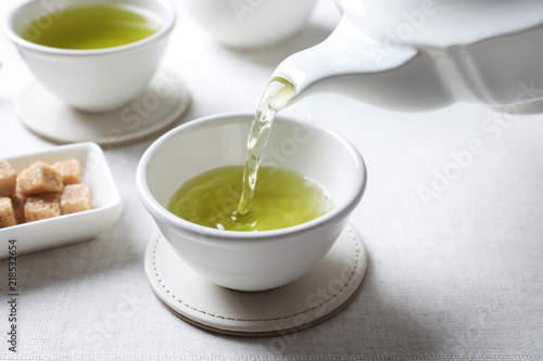 Pouring green tea into white porcelain cup on light table