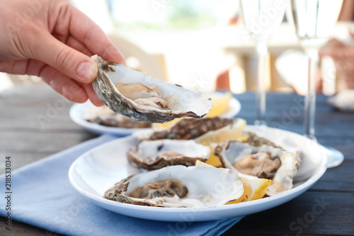 Woman with fresh oyster over plate, focus on hand