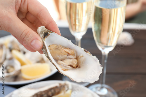 Woman with fresh oyster over table, focus on hand