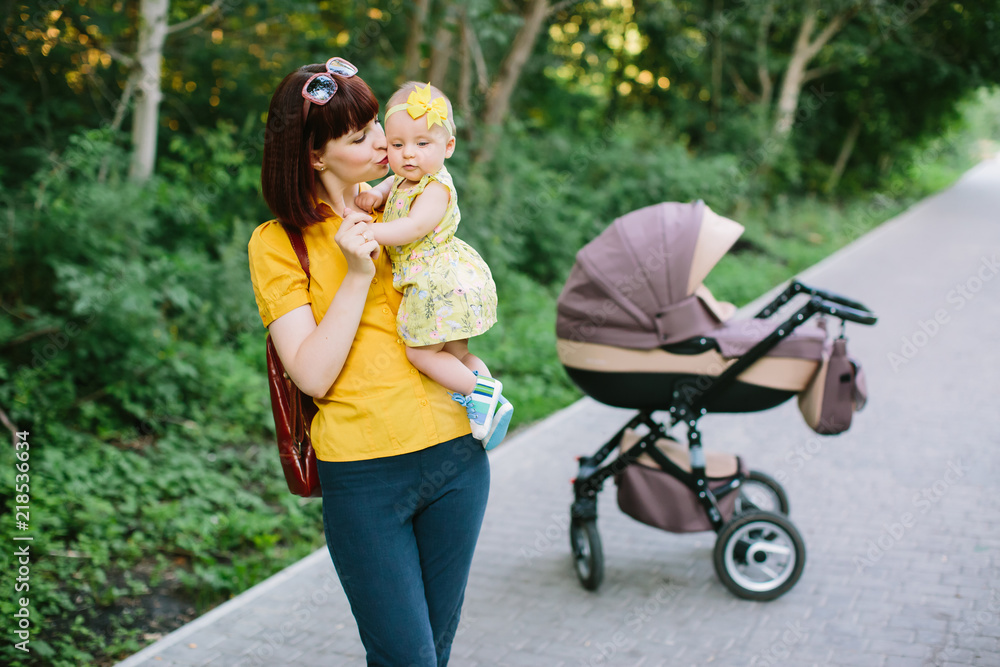 Young mother walking with baby carriage in the park, evening sun shine Young mother walking with baby carriage in the park, evening sun shine