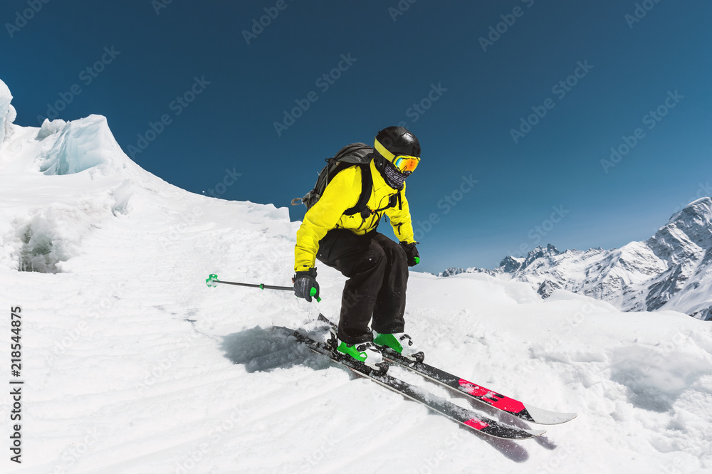Professional skier at the speed before jumping from the glacier in winter against the blue sky and mountains Professional skier at the speed before jumping from the glacier in winter against the blue sky and mountains