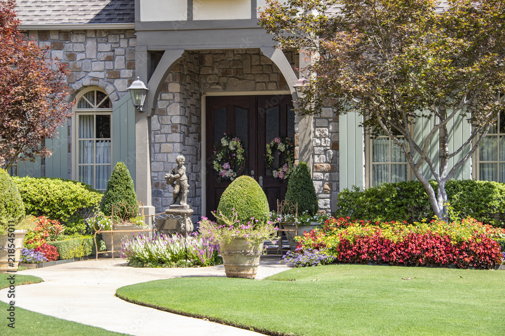 Obraz premium Entrance to upscale rock house with beautiful landscaping and a statue and wreaths and benches beside front porch