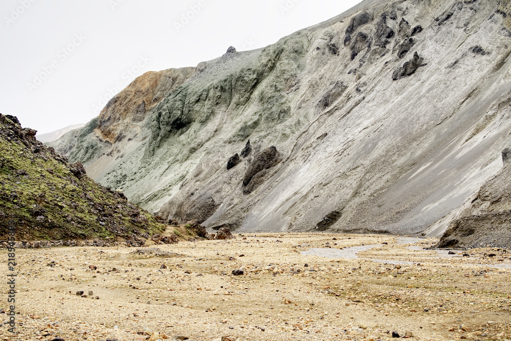 Fototapeta premium Pale Gray-Green Rhyolite Ridge with Dark Erosion Gullies Above a Sandy Valley in the Rainbow Mountains, Iceland