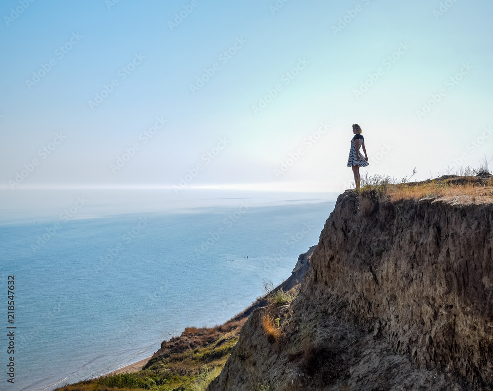 The girl is standing on a cliff near the sea.